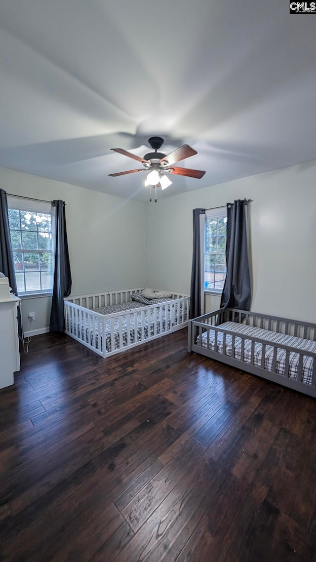 unfurnished bedroom featuring a nursery area, multiple windows, and hardwood / wood-style flooring