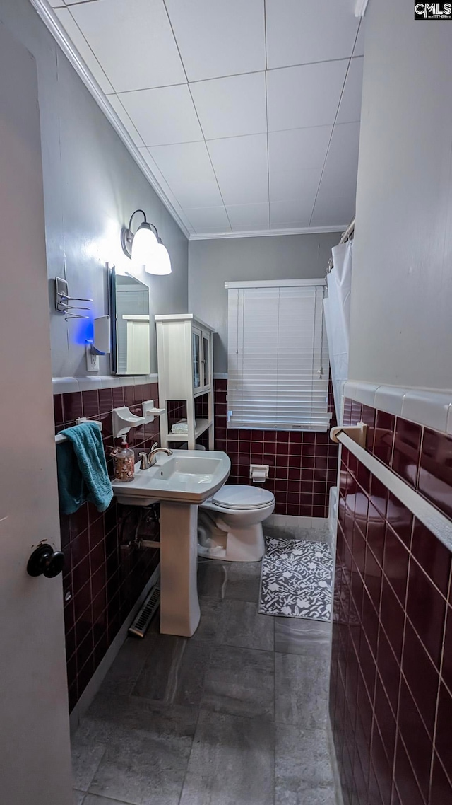 full bathroom featuring tile walls, wainscoting, toilet, crown molding, and a sink