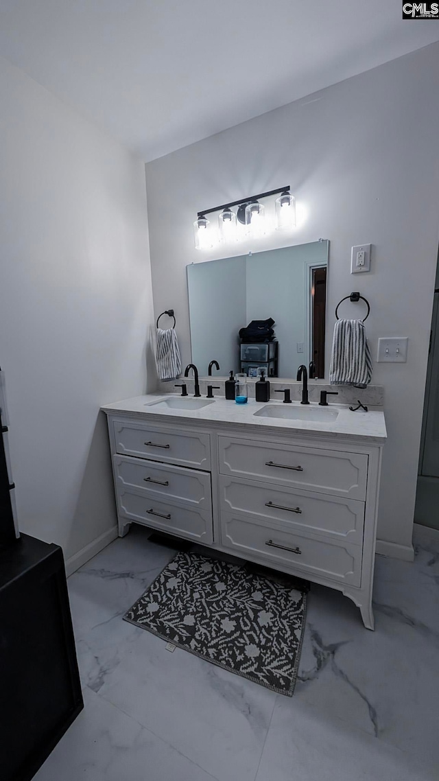 full bathroom featuring marble finish floor, a sink, baseboards, and double vanity