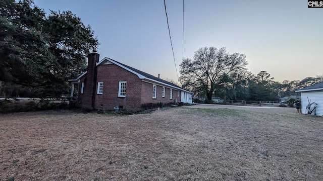 view of property exterior featuring a chimney, fence, and brick siding