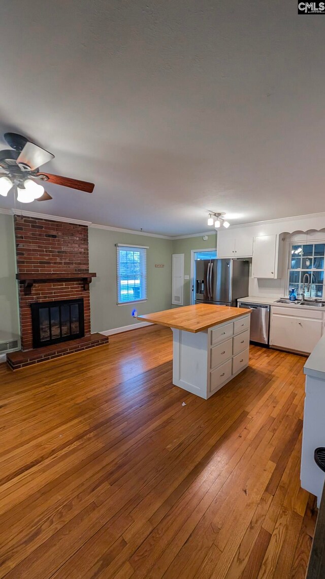 kitchen with white cabinets, appliances with stainless steel finishes, ornamental molding, a fireplace, and wooden counters