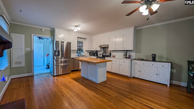 kitchen with butcher block counters, ornamental molding, stainless steel appliances, under cabinet range hood, and white cabinetry