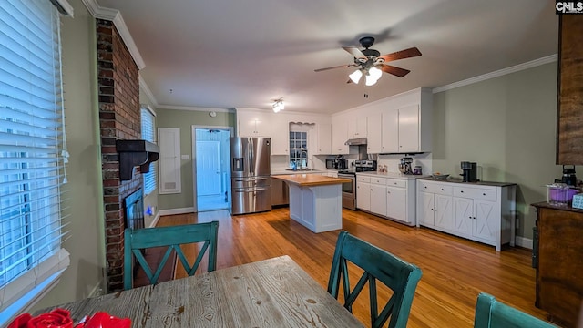 kitchen with under cabinet range hood, stainless steel appliances, a fireplace, white cabinetry, and light wood finished floors