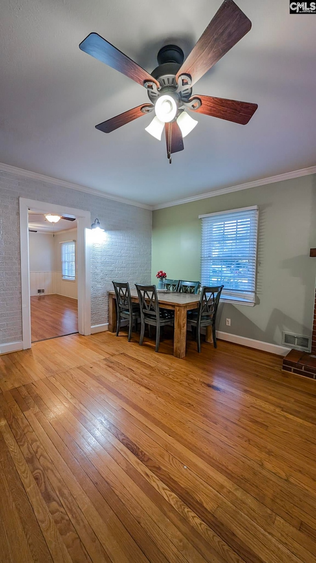 dining space featuring ornamental molding, wood-type flooring, baseboards, and brick wall