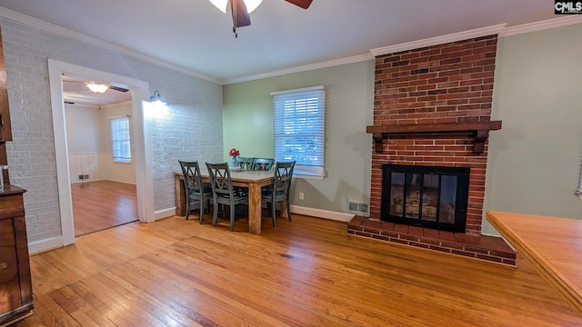 dining space with a ceiling fan, ornamental molding, a brick fireplace, plenty of natural light, and hardwood / wood-style floors