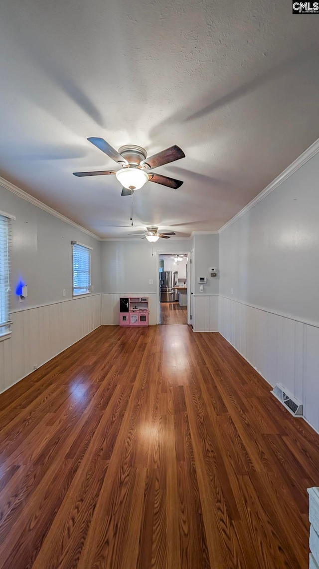 unfurnished living room featuring a textured ceiling, a wainscoted wall, wood finished floors, visible vents, and ornamental molding