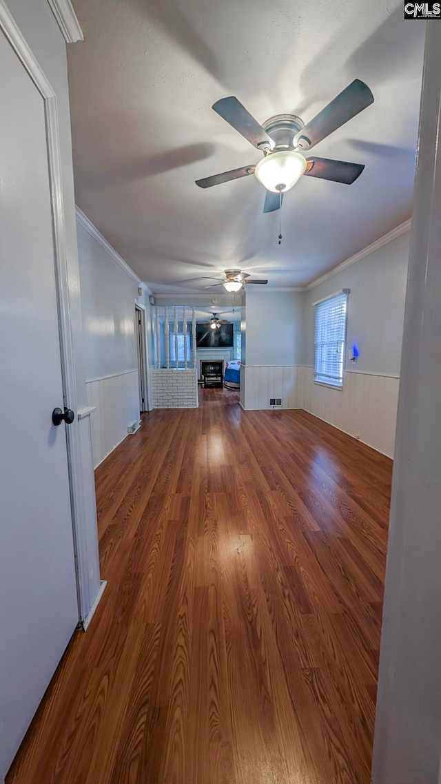 unfurnished living room featuring a wainscoted wall, crown molding, visible vents, and wood finished floors