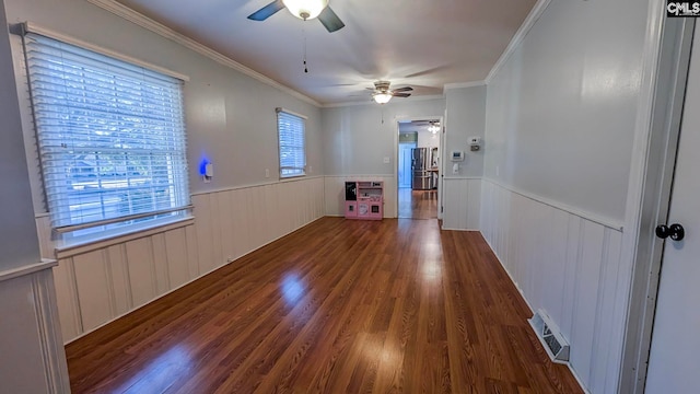 unfurnished room with a wainscoted wall, wood finished floors, visible vents, a ceiling fan, and ornamental molding