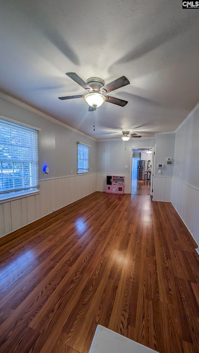 unfurnished living room featuring ornamental molding, a wainscoted wall, ceiling fan, and wood finished floors