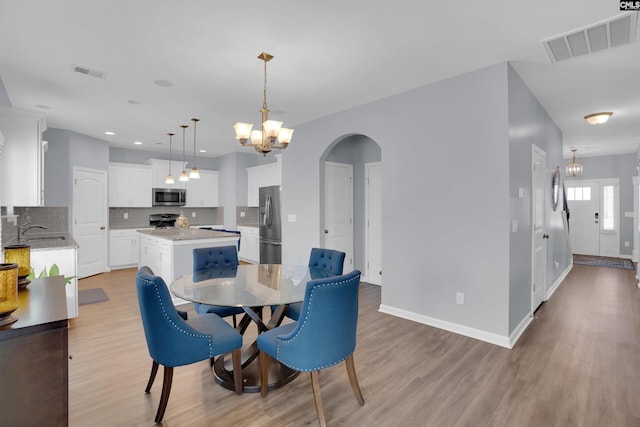 dining area featuring arched walkways, visible vents, and light wood-style floors