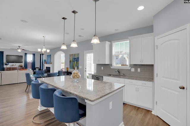 kitchen featuring a fireplace, backsplash, stainless steel dishwasher, white cabinetry, and a kitchen island