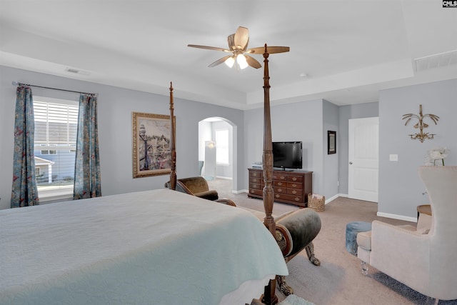 carpeted bedroom with baseboards, visible vents, arched walkways, and a tray ceiling