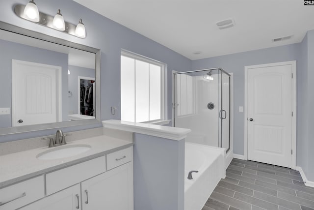 bathroom with a stall shower, visible vents, a garden tub, a walk in closet, and vanity