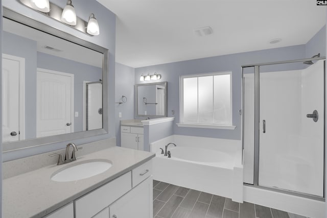 full bath with a stall shower, visible vents, two vanities, a sink, and a bath