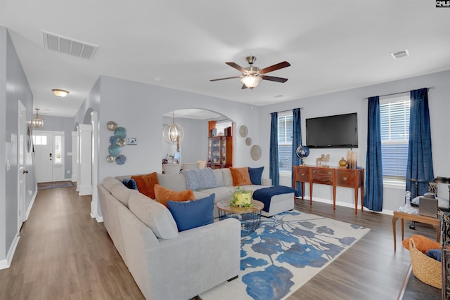 living room featuring arched walkways, ceiling fan with notable chandelier, wood finished floors, and visible vents