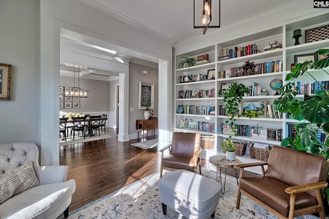 sitting room featuring built in shelves, crown molding, an inviting chandelier, wood finished floors, and baseboards