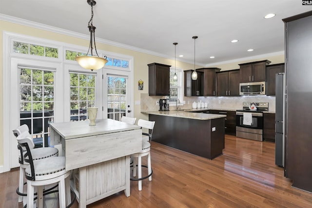 kitchen with dark brown cabinetry, stainless steel appliances, dark wood-type flooring, a peninsula, and a sink