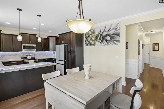 kitchen featuring dark brown cabinetry, wood finished floors, stainless steel appliances, crown molding, and backsplash