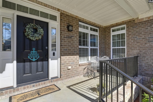 view of exterior entry featuring covered porch and brick siding