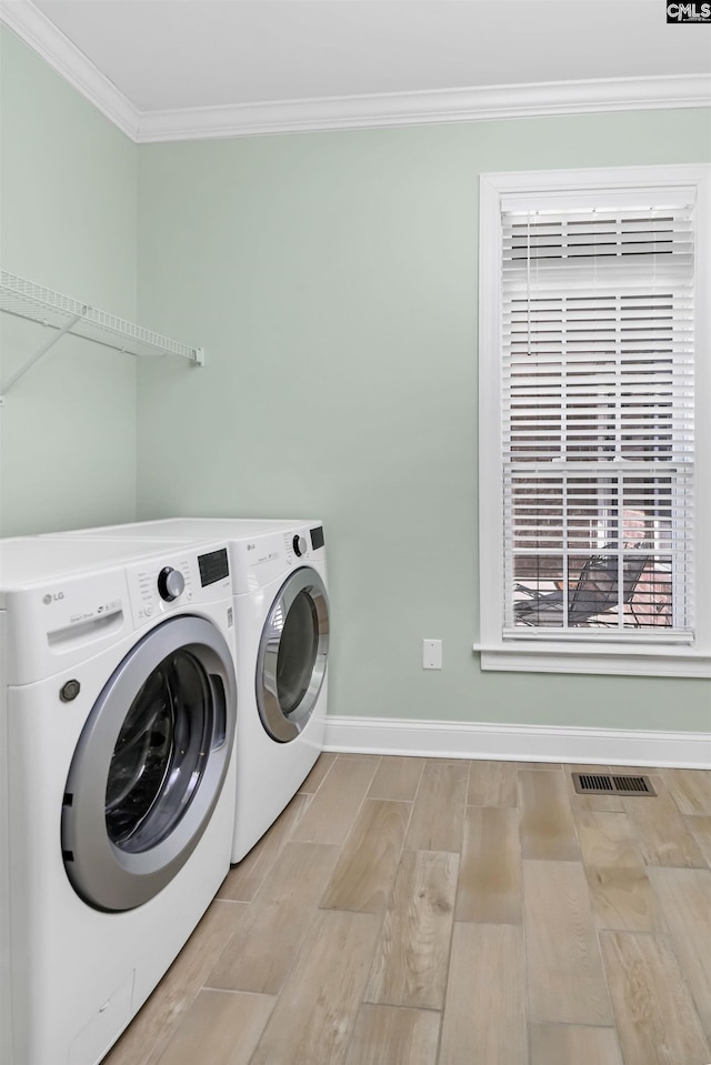 clothes washing area featuring laundry area, baseboards, washer and dryer, ornamental molding, and light wood finished floors