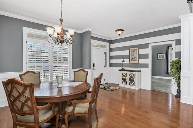 dining area with a wainscoted wall, ornamental molding, wood finished floors, and an inviting chandelier