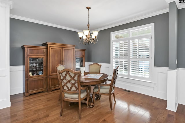 dining area featuring a chandelier, a wainscoted wall, ornamental molding, and wood finished floors