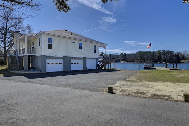 view of home's exterior featuring a garage, a water view, driveway, and stairs