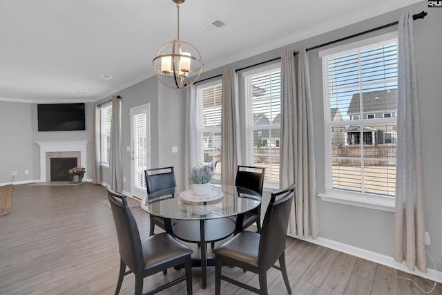 dining area featuring a fireplace with flush hearth, wood finished floors, visible vents, baseboards, and ornamental molding