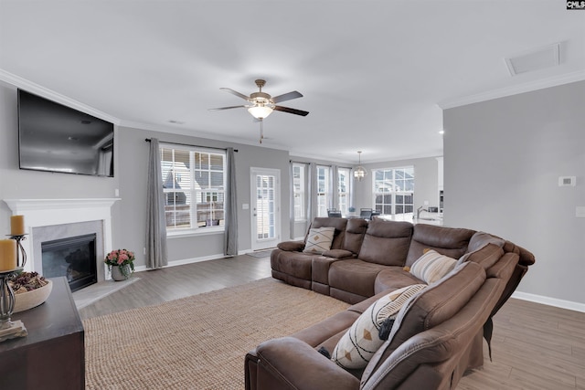 living room featuring light wood finished floors, plenty of natural light, a high end fireplace, and crown molding