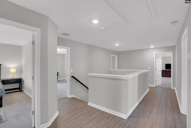 hallway featuring attic access, visible vents, an upstairs landing, and wood finished floors