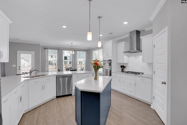 kitchen with a sink, light countertops, appliances with stainless steel finishes, wall chimney exhaust hood, and crown molding