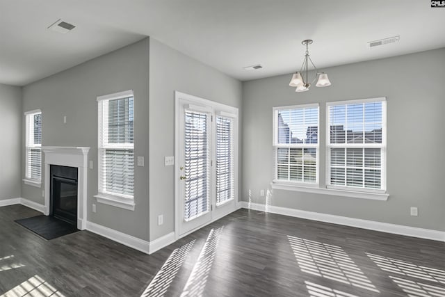 unfurnished dining area with baseboards, a notable chandelier, visible vents, and dark wood-type flooring