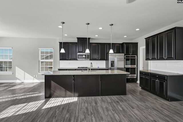 kitchen with decorative backsplash, a large island, appliances with stainless steel finishes, hanging light fixtures, and a sink