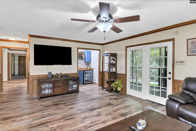 living area featuring ceiling fan, beverage cooler, wood finished floors, wainscoting, and crown molding