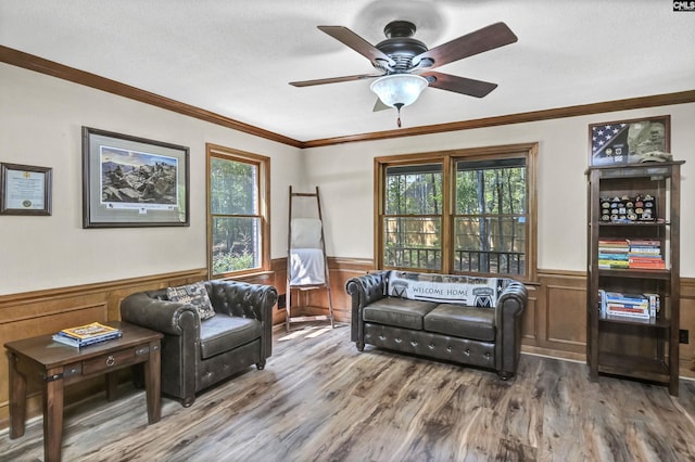 living area with ornamental molding, wainscoting, wood finished floors, and a ceiling fan