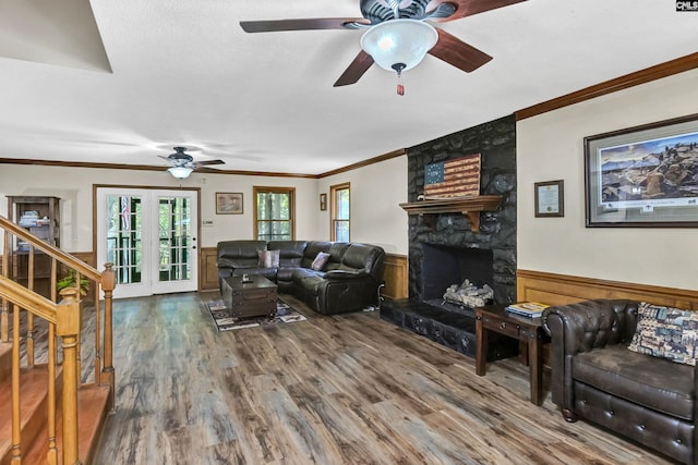 living area featuring a wainscoted wall, stairway, ornamental molding, wood finished floors, and a stone fireplace