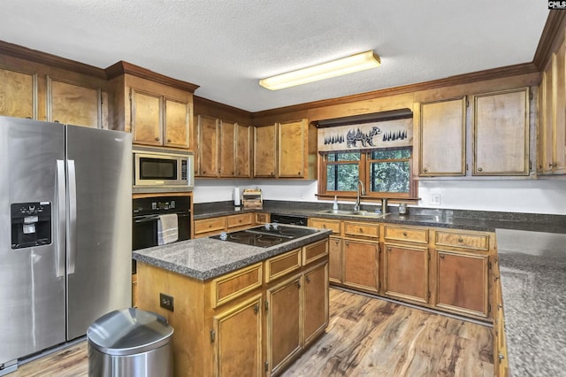 kitchen with a textured ceiling, a sink, black appliances, light wood finished floors, and brown cabinetry