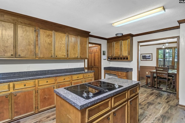 kitchen with dark wood finished floors, dark countertops, ornamental molding, brown cabinetry, and black electric cooktop