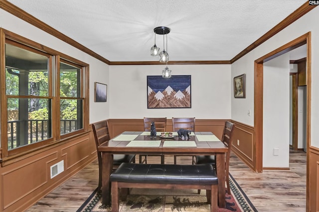 dining space with light wood-style flooring, a wainscoted wall, visible vents, and a textured ceiling