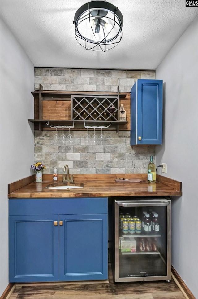 bar featuring wine cooler, wood finished floors, a sink, a textured ceiling, and indoor wet bar