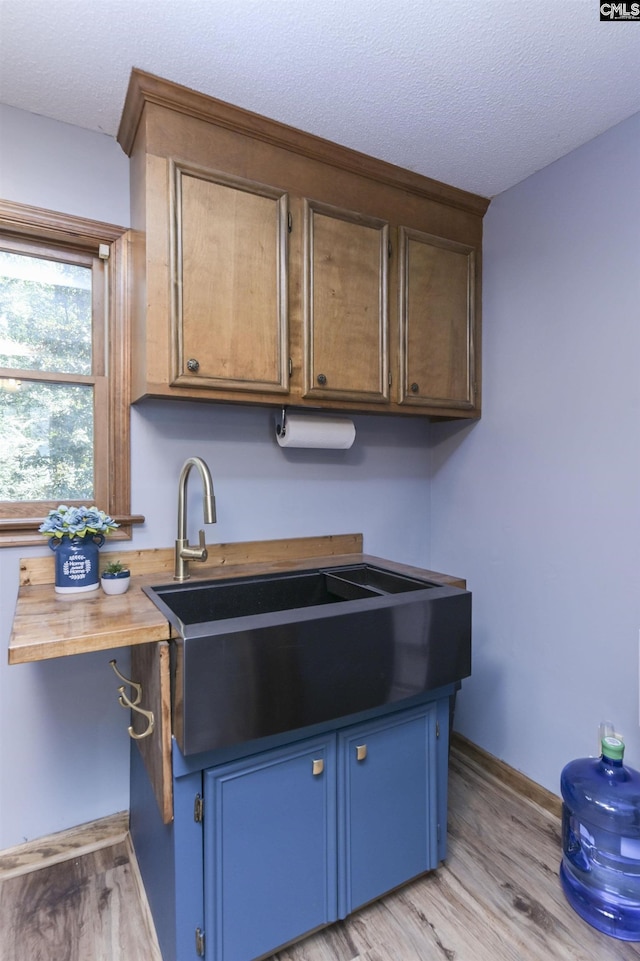 kitchen with blue cabinetry, baseboards, light wood finished floors, and a textured ceiling