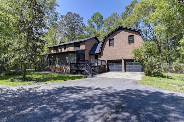 view of front of house with brick siding, an attached garage, a gambrel roof, fence, and driveway