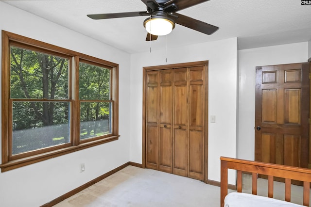 unfurnished bedroom with a closet, light colored carpet, ceiling fan, a textured ceiling, and baseboards