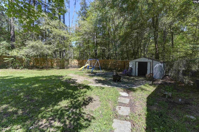 view of yard featuring a storage unit, a playground, a fenced backyard, and an outdoor structure