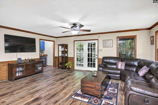 living room featuring a wainscoted wall, ceiling fan, wood finished floors, crown molding, and french doors