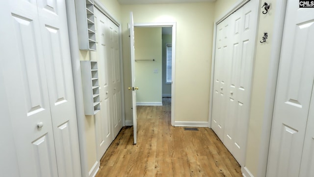 hall featuring visible vents, light wood-type flooring, and baseboards