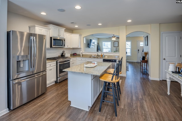 kitchen with white cabinetry, appliances with stainless steel finishes, arched walkways, and a center island