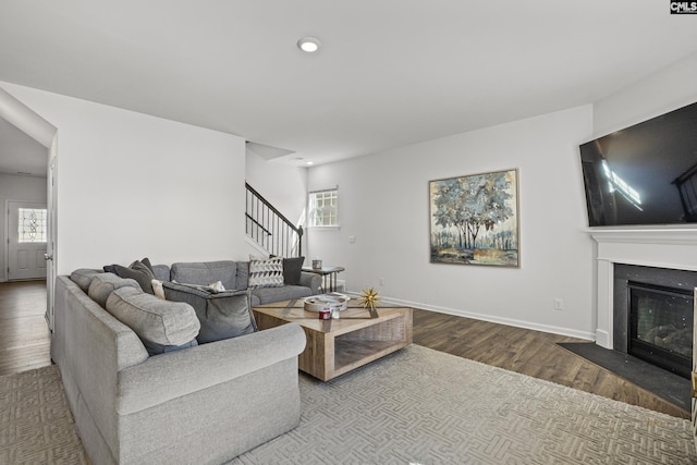 living area with recessed lighting, a fireplace with flush hearth, wood finished floors, baseboards, and stairway