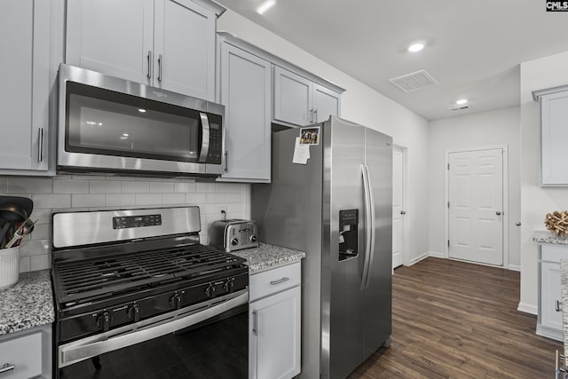 kitchen with light stone counters, stainless steel appliances, visible vents, backsplash, and dark wood-type flooring