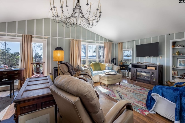 living area featuring a chandelier, vaulted ceiling, wood finished floors, and a glass covered fireplace